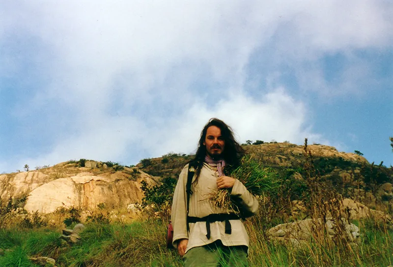 Rainer Weber jung, auf einem Berg stehend mit Kräuter im Arm.